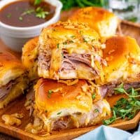 Square image of stacked French Dip Sliders on wooden plate.