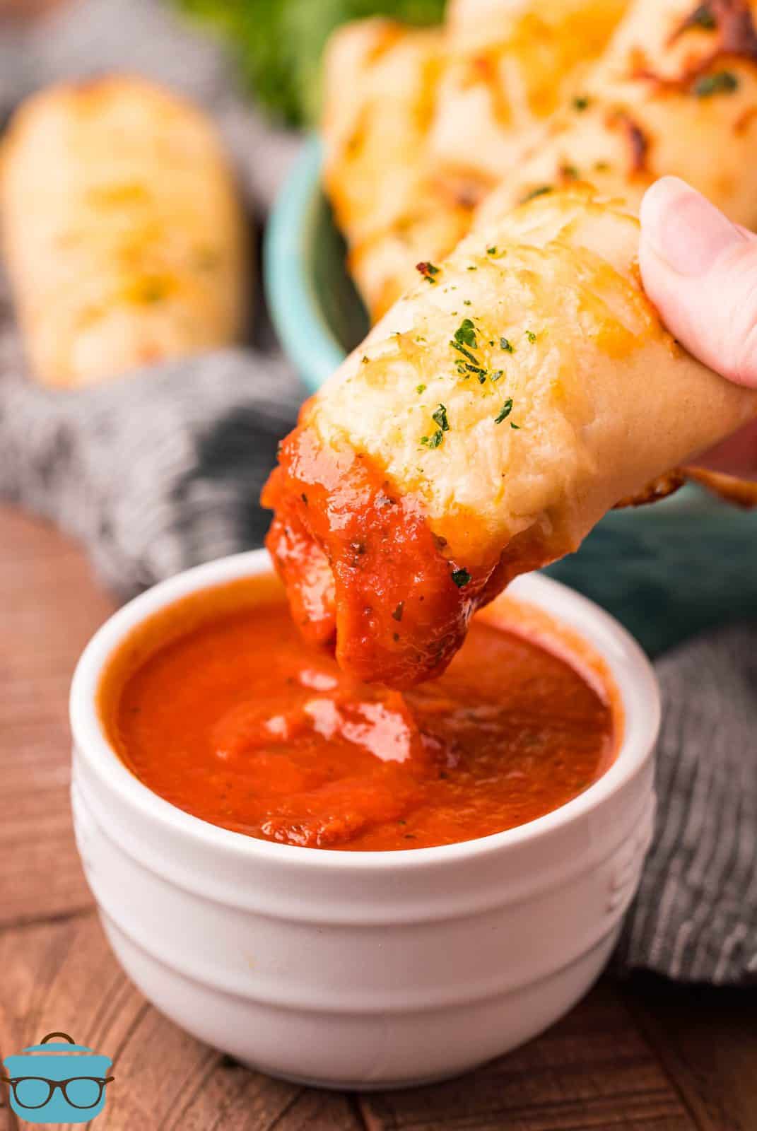 Hand dipping one Cheese Stuffed Breadstick in dipping sauce.