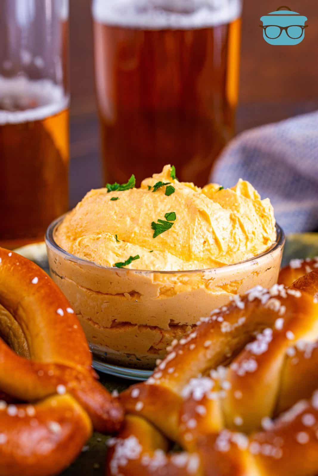 Beer Cheese Dip in bowl with pretzels and beer around it.