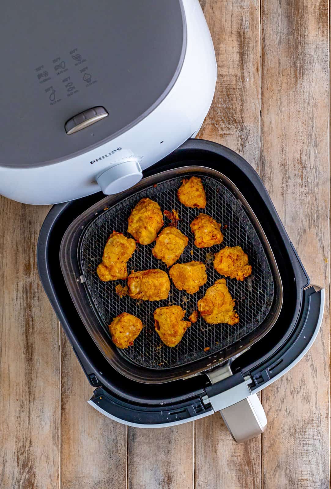 fully cooked chicken nuggets shown in the bottom of an air fryer basket.