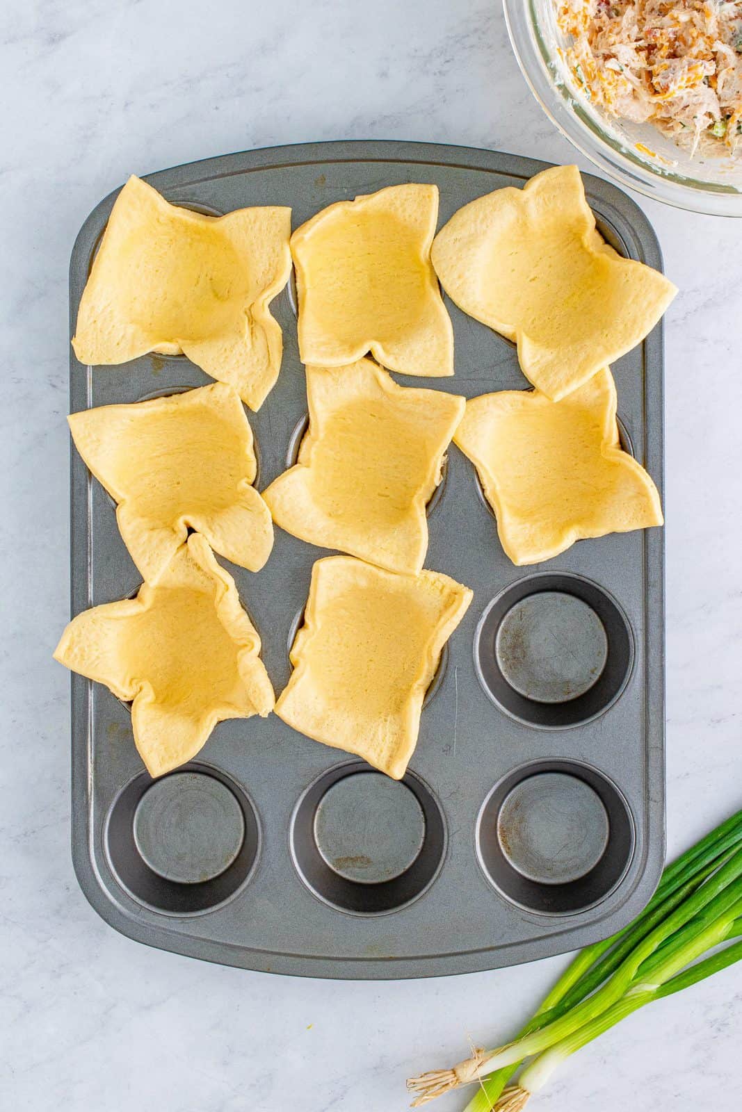 Crescent roll dough sheet cut and placed in muffin tin.