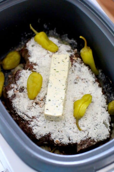 ranch dressing, onion soup mix and a stick of butter shown on a pot roast in a crock pot.