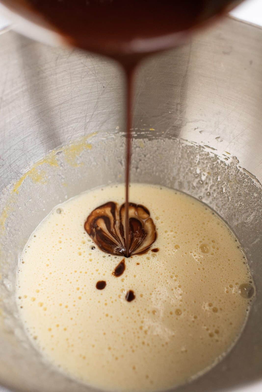 Chocolate mixture, sugar, vanilla, and eggs being beaten together in body of stand mixer.