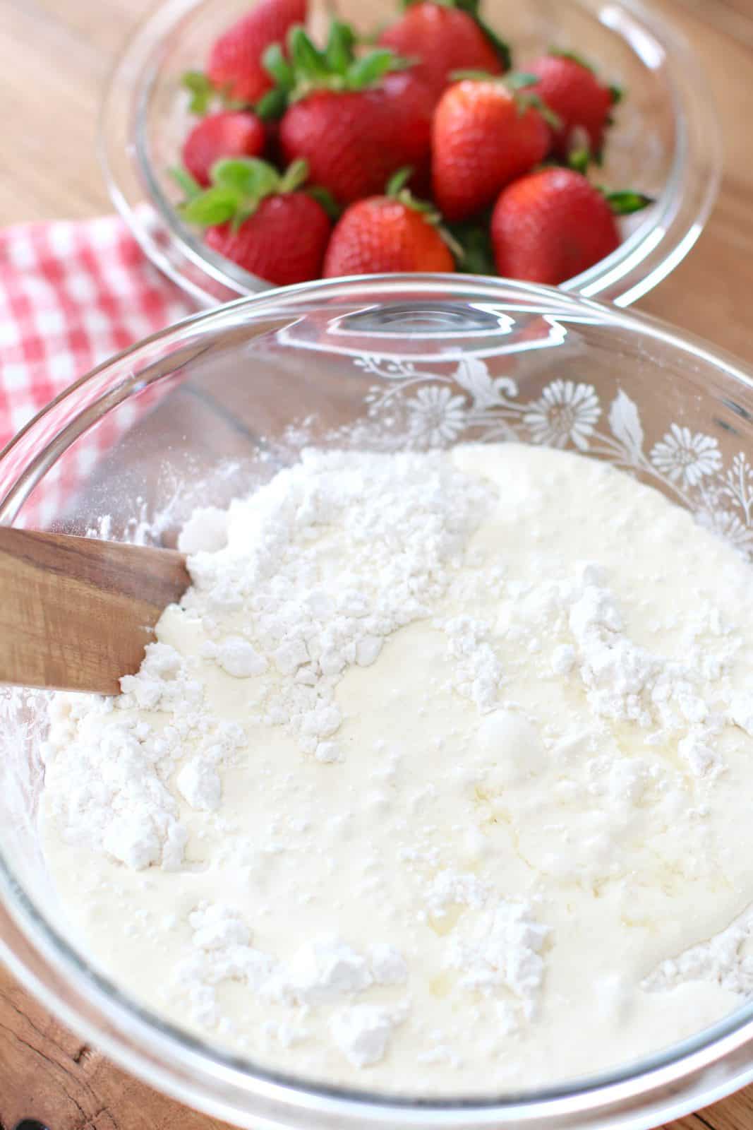 heavy cream and strawberry extract poured into glass bowl that holds the all purpose flour mixture.