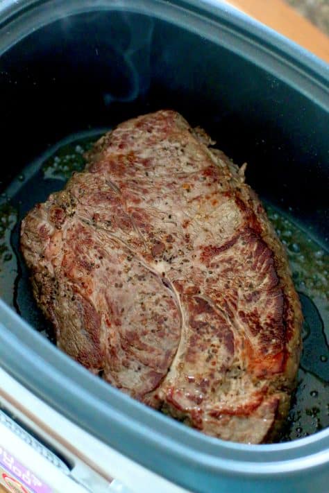 browned chuck roast shown in an oval slow cooker.
