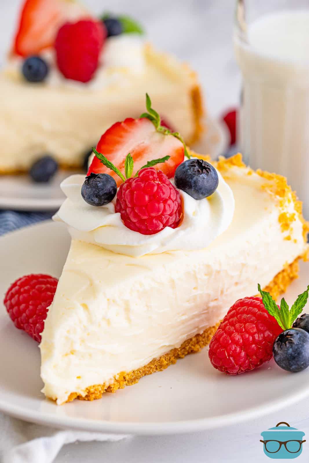 Slice of No-Bake Cheesecake on white plate topped with whipped cream and fruit.