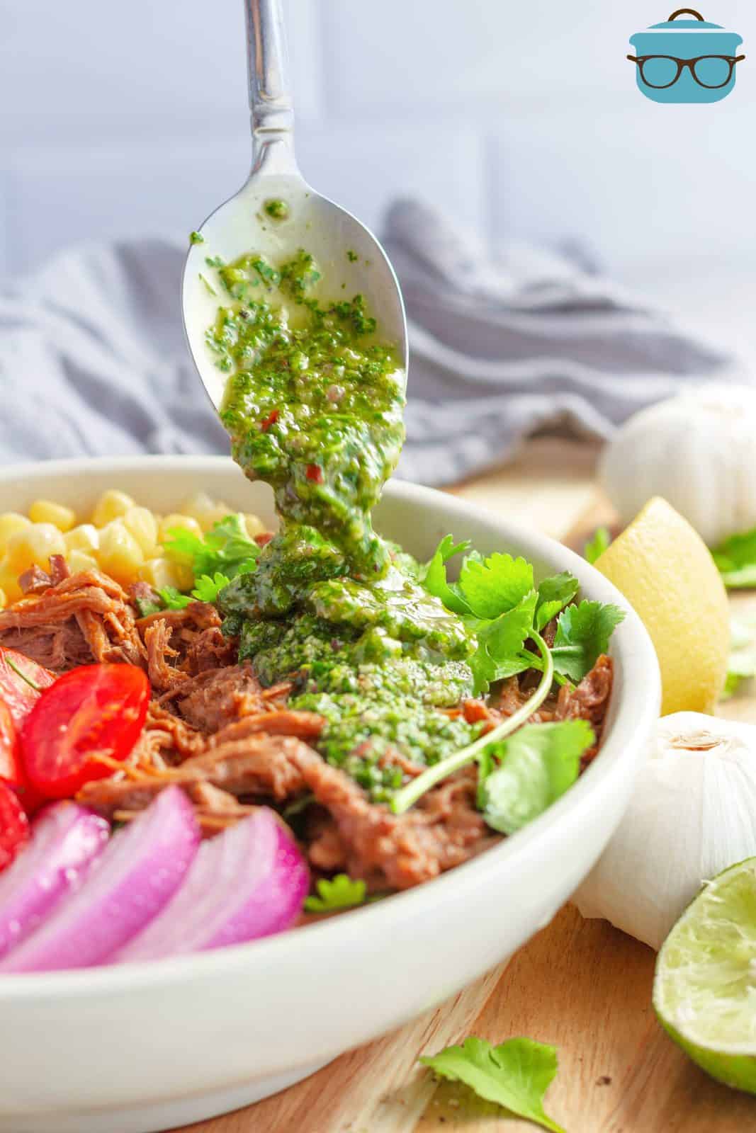 Chimichurri Sauce being spooned over a bowl of meat and vegetables.