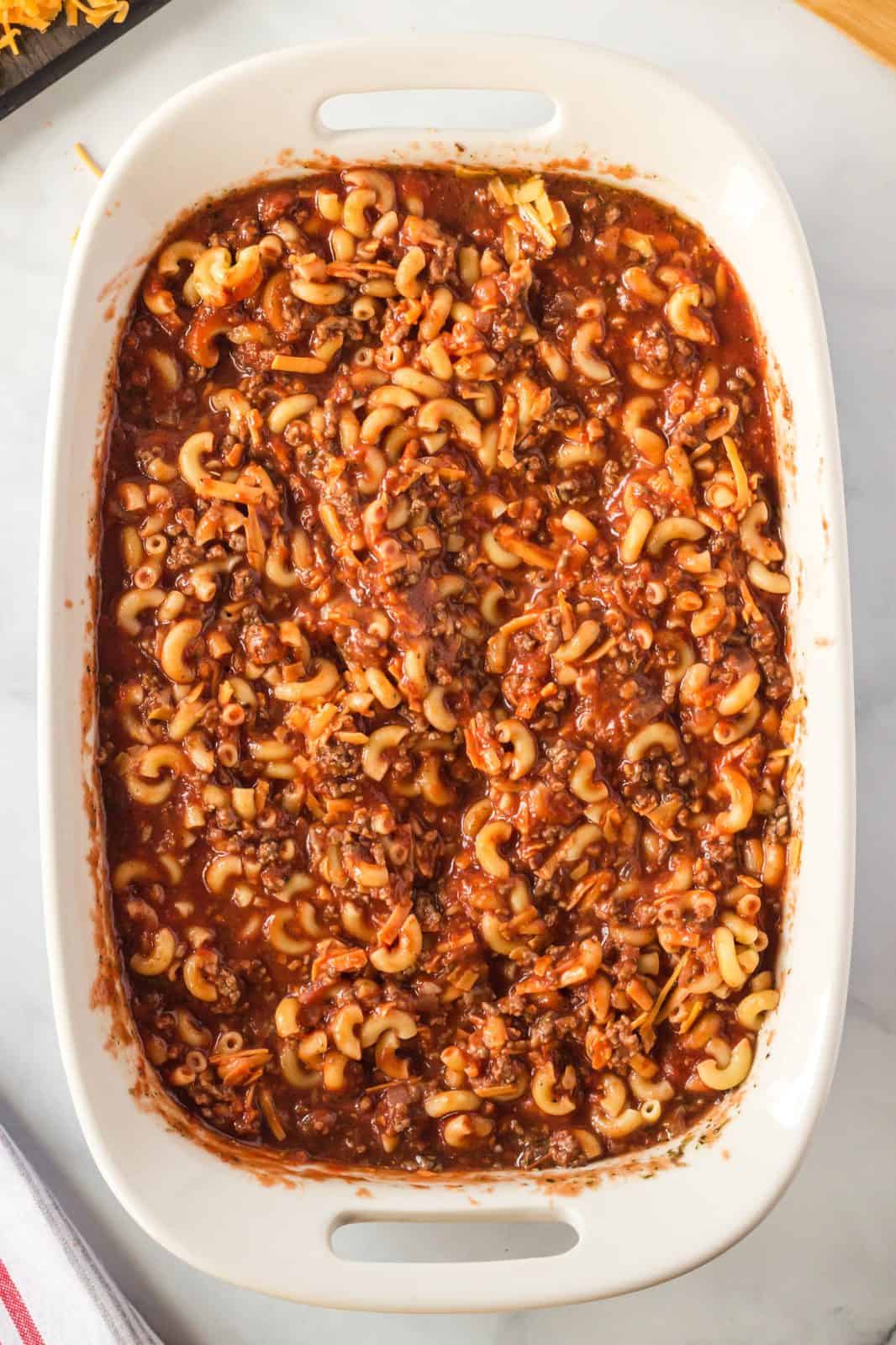 Ground beef mixture with cheese and pasta added to baking dish.