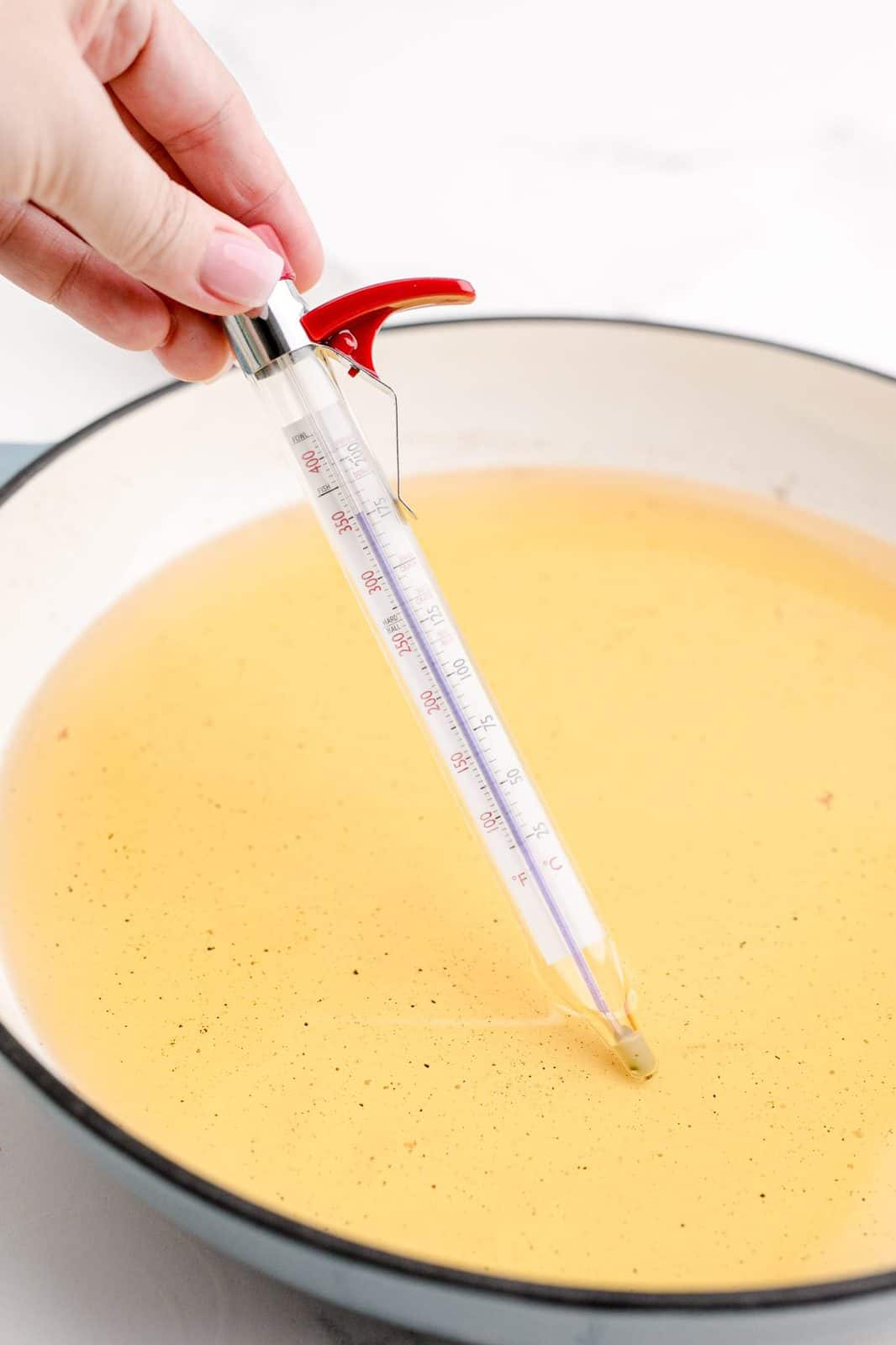 Hand holding candy thermometer checking oil temperature.
