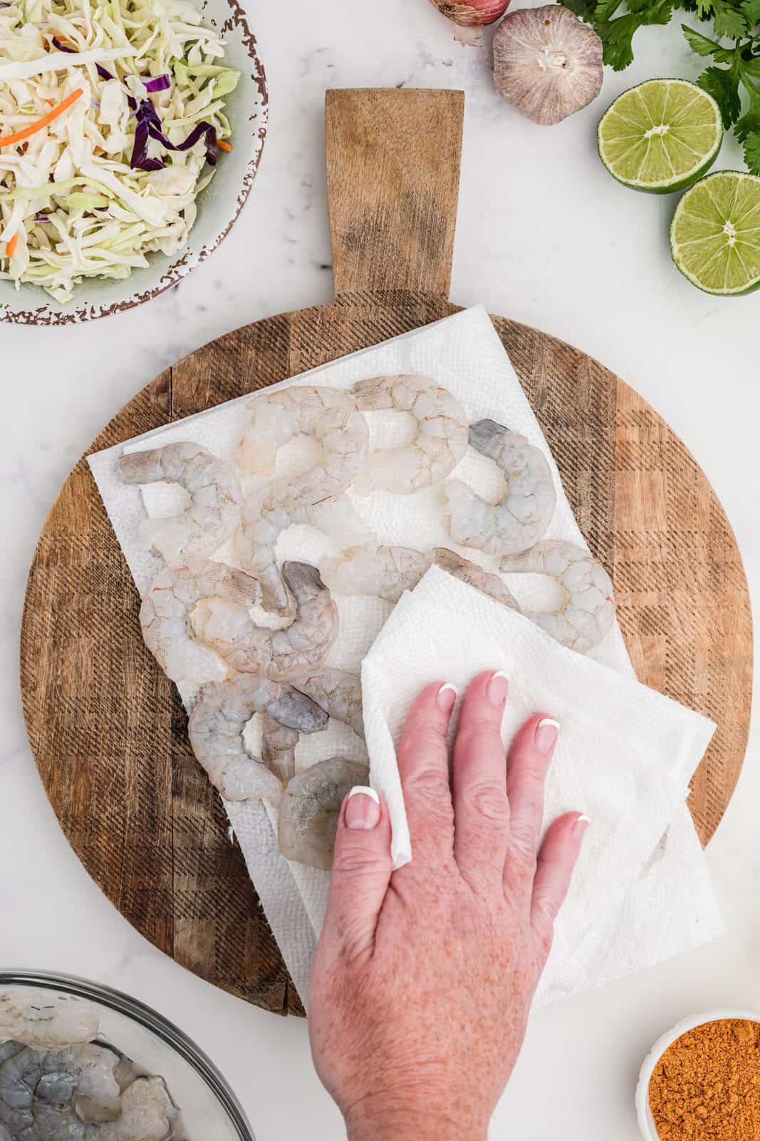 Hand patting dry shrimp on cutting board with paper towel.