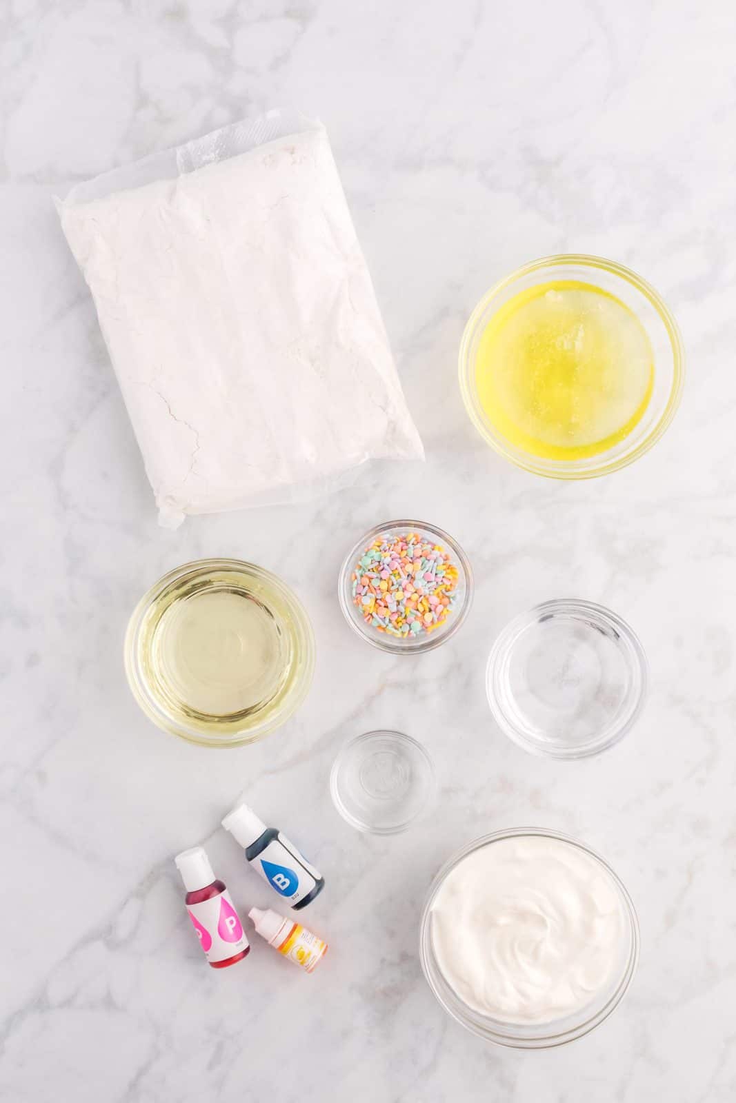 Ingredients needed: white cake mix, water, egg whites, vegetable oil, sour cream, vanilla extract, blue, pink, and yellow food coloring, pastel colored sprinkles, butter, powdered sugar, salt and heavy cream.