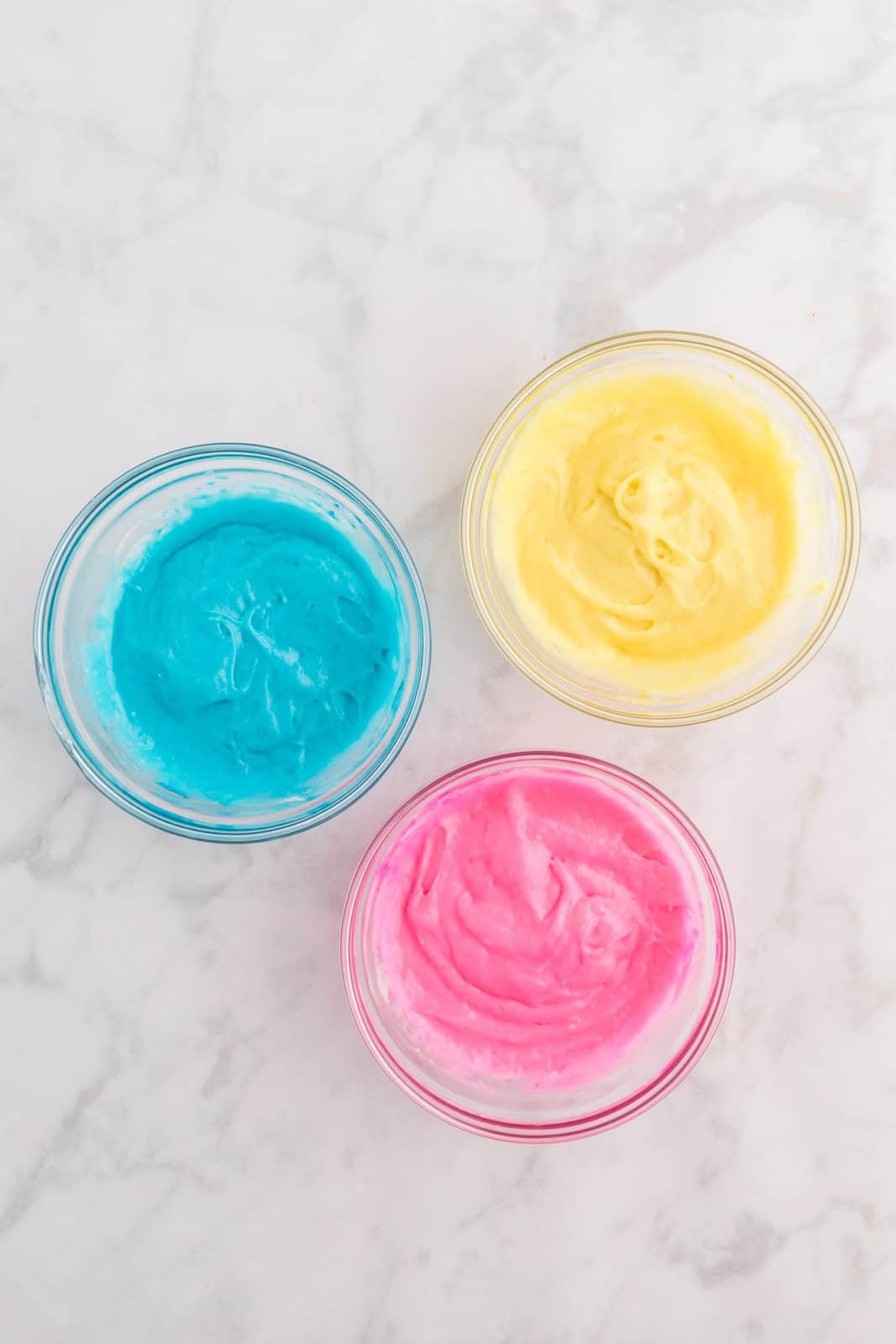 Remaining cake mix separated out into 3 bowls and colored blue, yellow and pink.