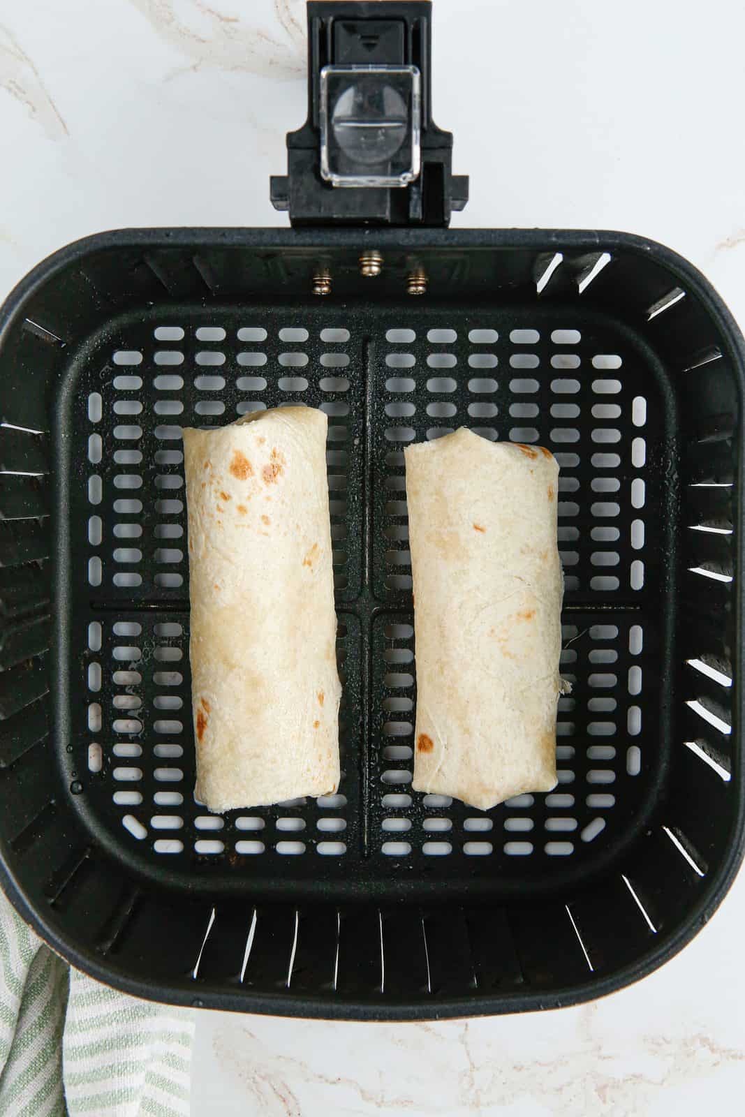 Folded chimichangas in air fryer basket.