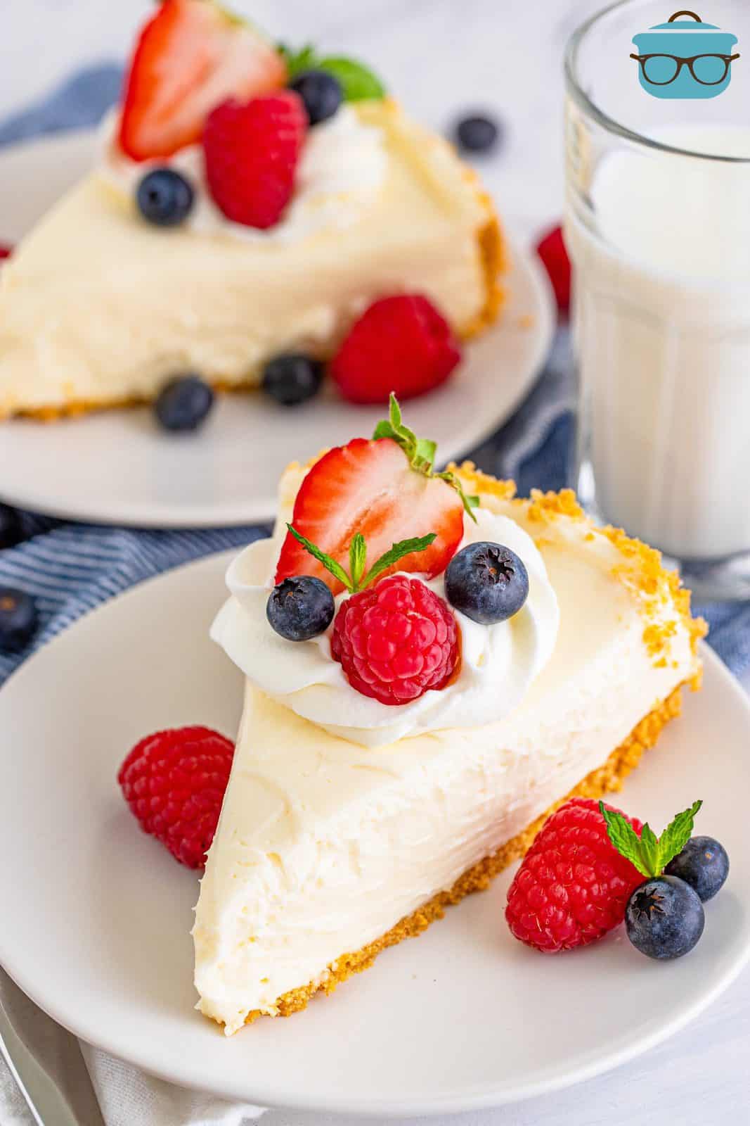 Sovraccarico di due fette di cheesecake senza cottura su un piatto bianco condito con panna montata e frutta.