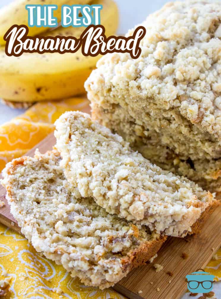 Banana Bread on a wooden board with two slices cut out and yellow bananas in the background.