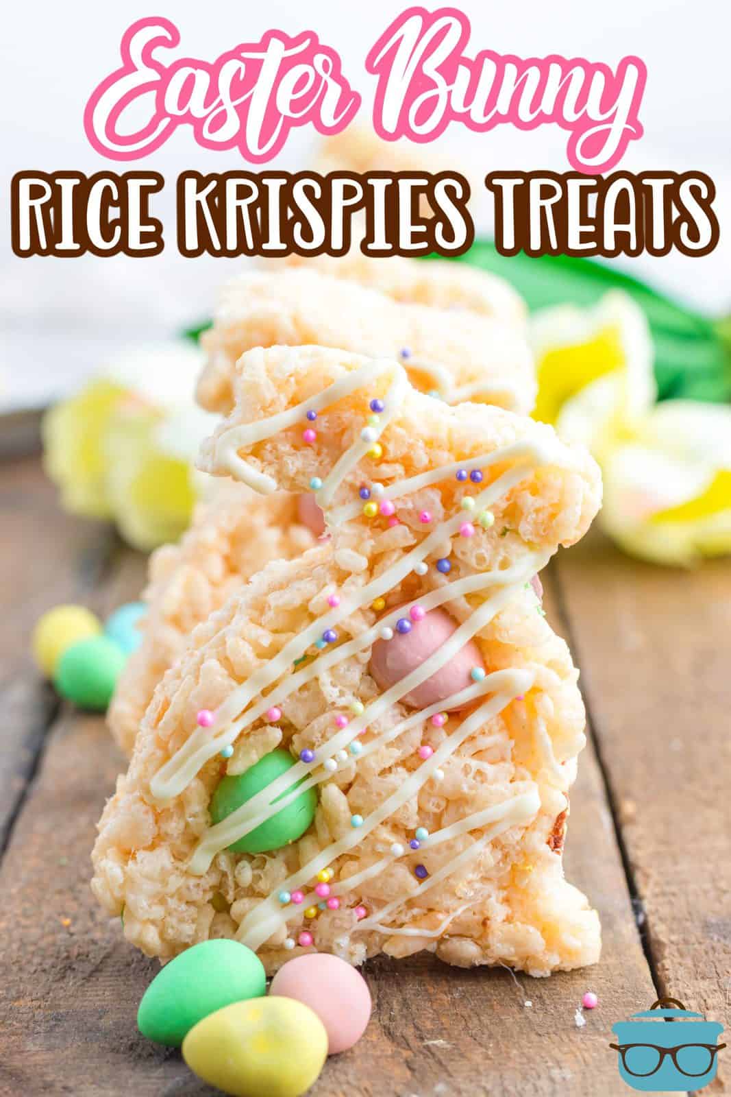 Pinterest image of Easter Bunny Rice Krispies Treats standing up in a row on wooden board with mini cadbury eggs.