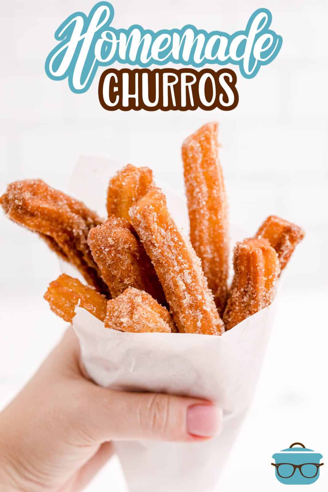 Hand holding Homemade Churros wrapped in parchment paper Pinterest image.