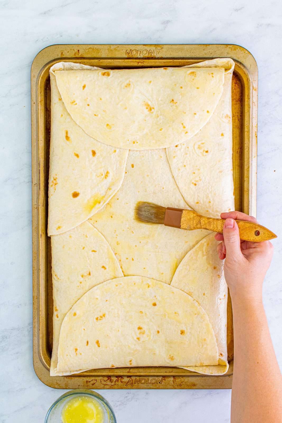 Butter being brushed over folded tortillas.