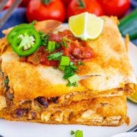 Square image of two stacked Sheet Pan Chicken Quesadillas on white plate with toppings.