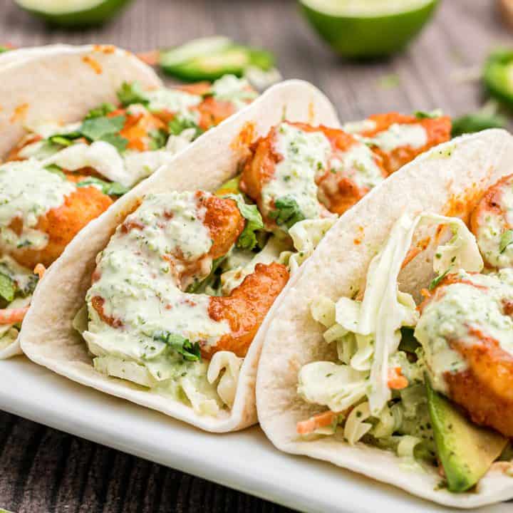 Close up square image of Shrimp Tacos on white platter showing shrimp and slaw.