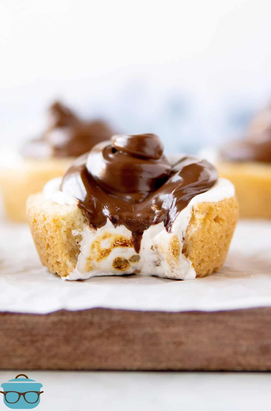 S'mores Cookie Cups on wooden board with parchment paper with bite taken out of it.