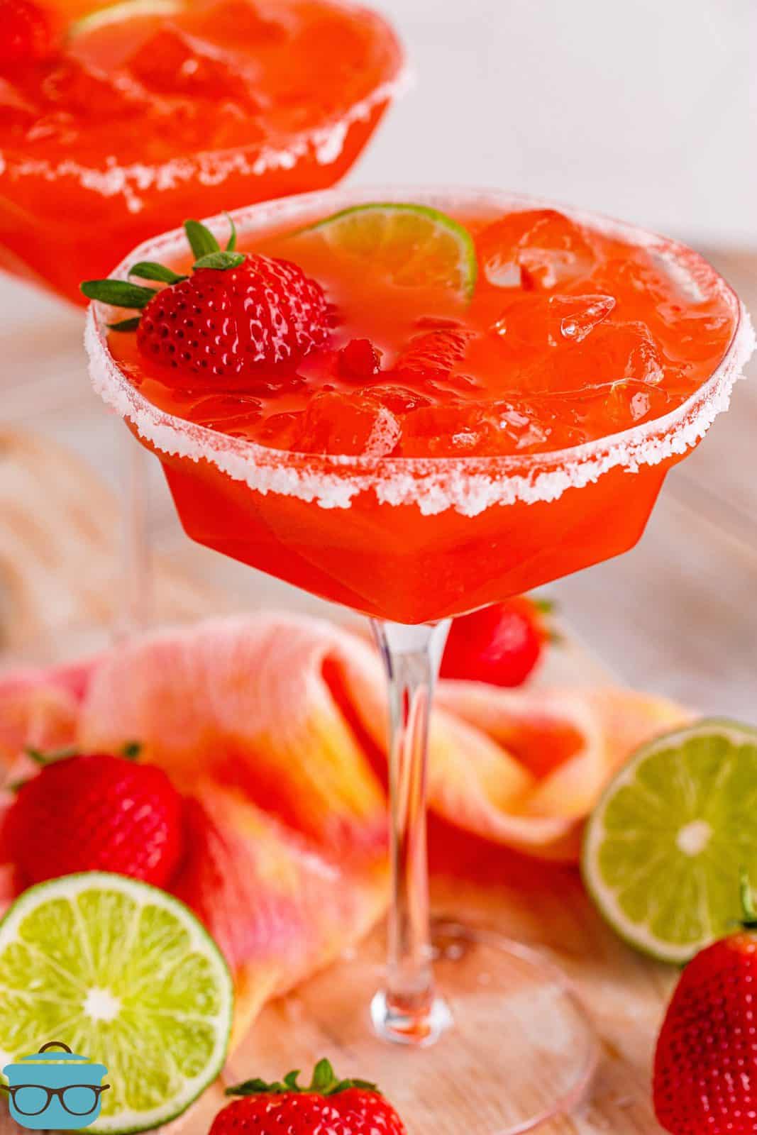 Strawberry Margaritas in two long stemmed glasses topped with a strawberry and lime slice.