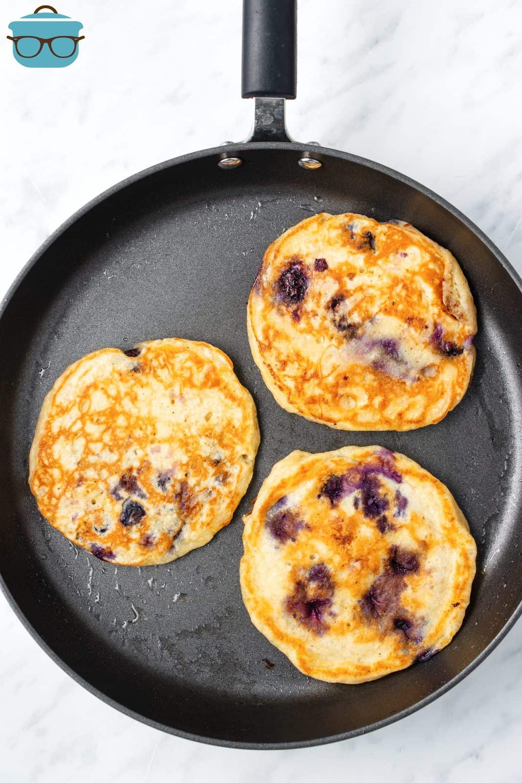 Blueberry Pancakes frying in pan.