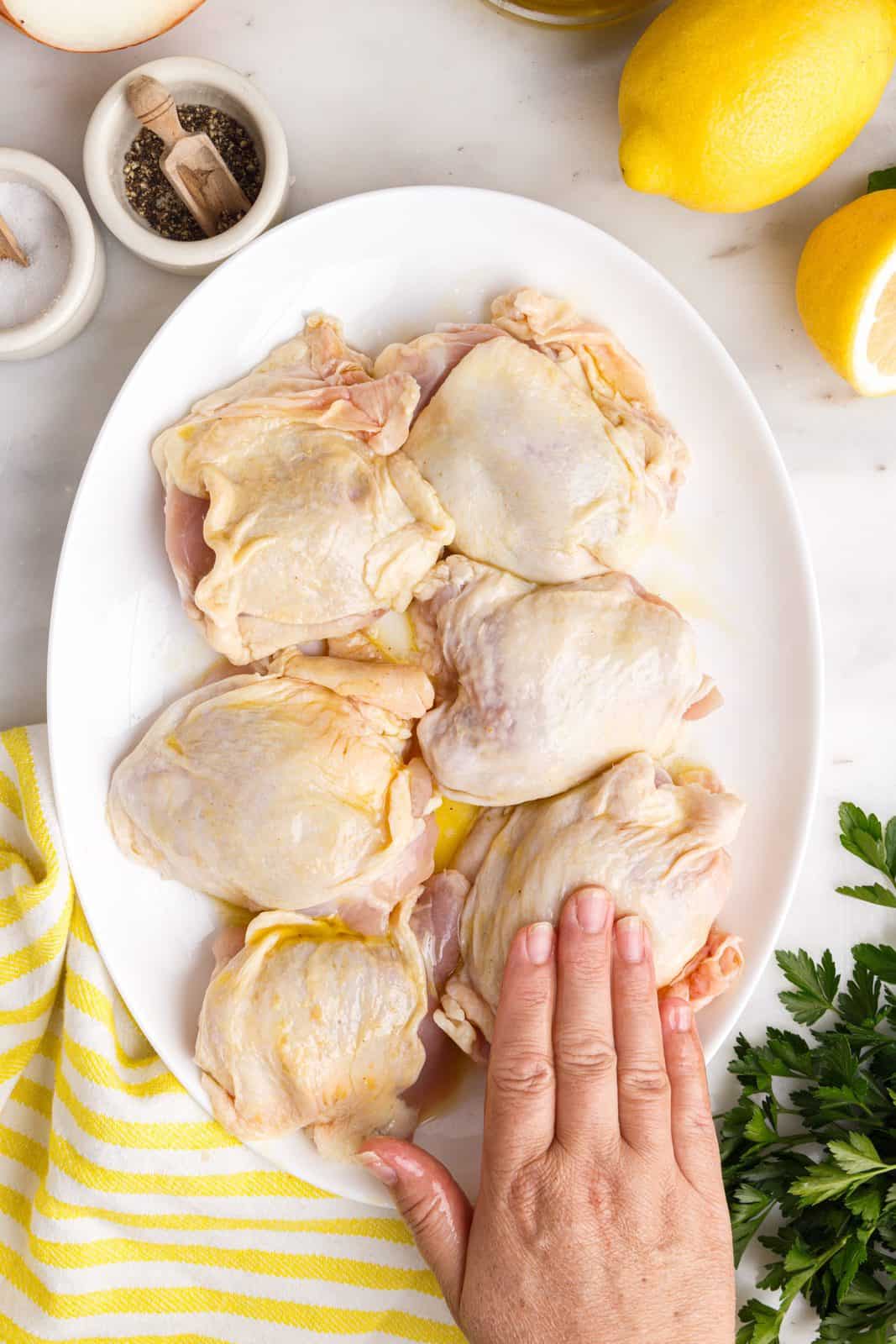 Hand rubbing oil and lemon mixture over chicken thighs.