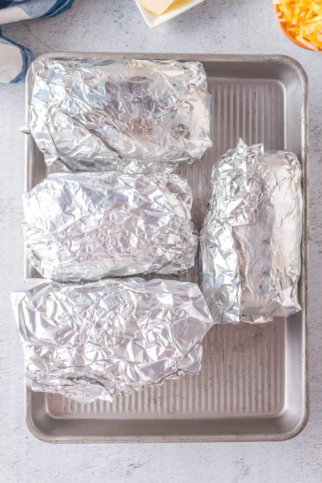 Potatoes wrapped in foil on baking sheet.