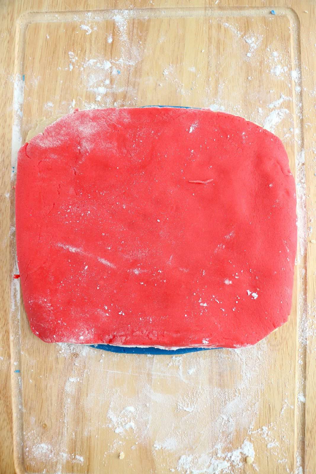 Red dough rolled out and placed on top of plain dough.