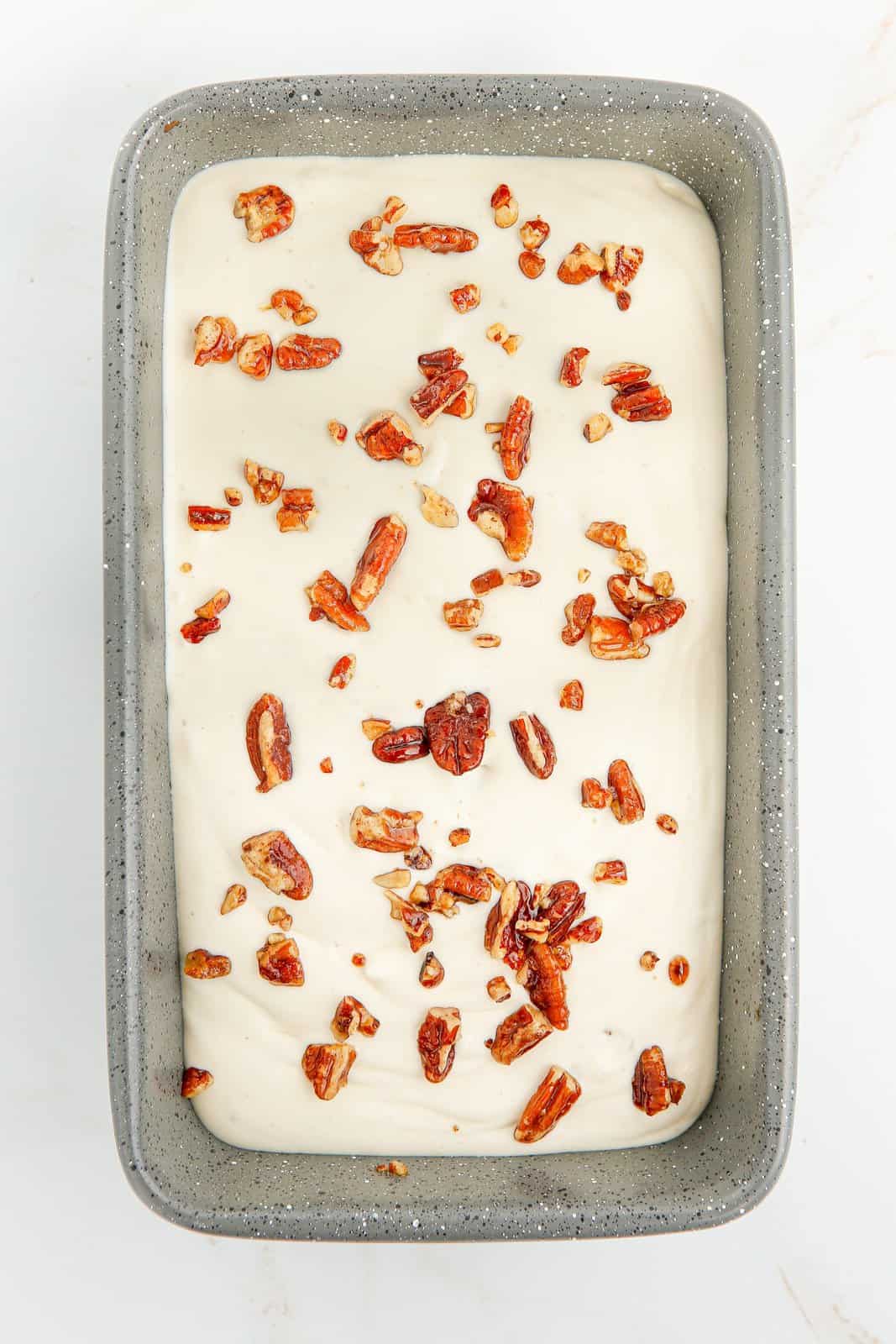 Ice cream mixture added to loaf pan topped with pecans.