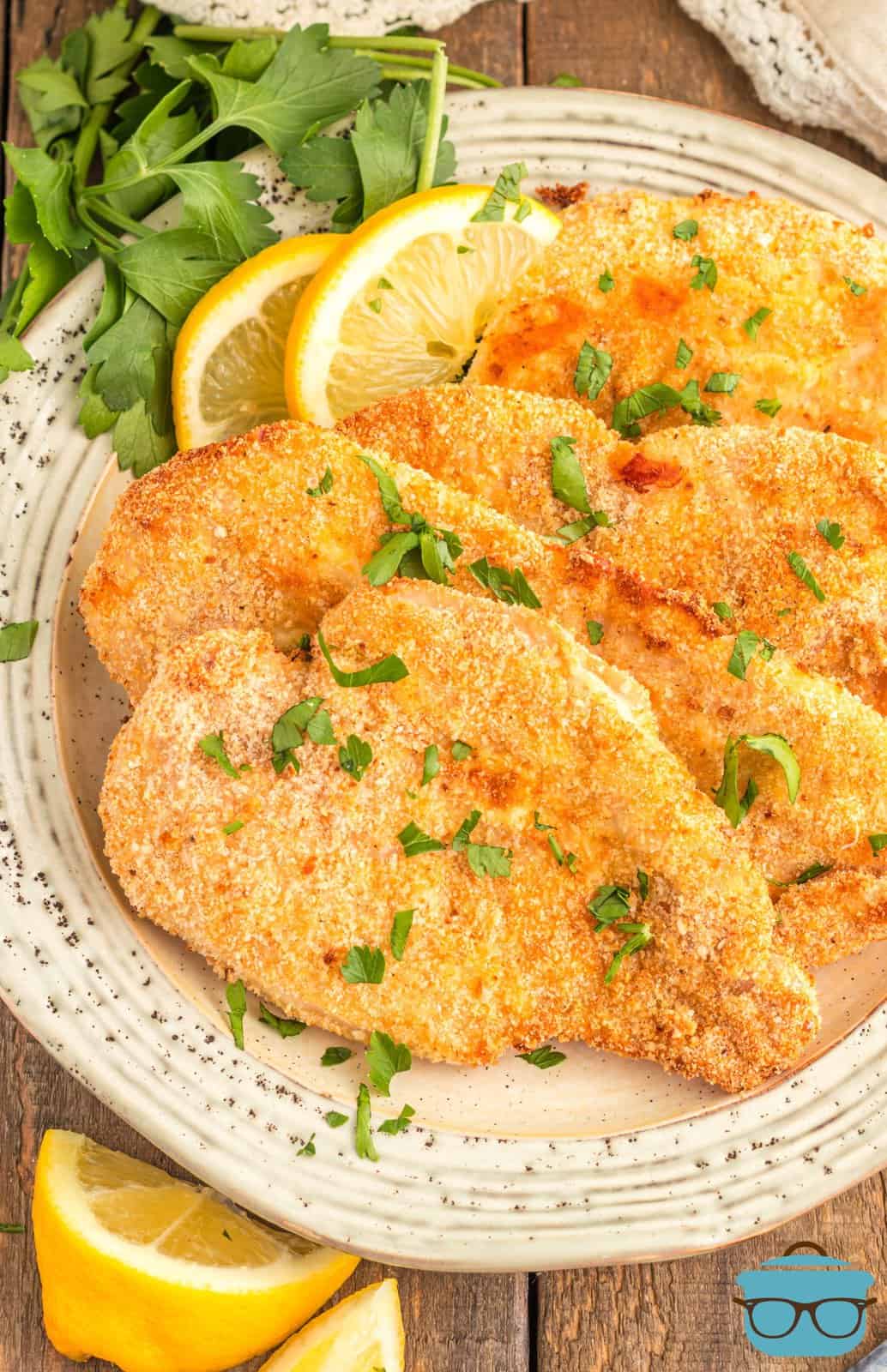 Overhead of layered Air Fryer Chicken Cutlets on plate with lemon wedges and parsley.