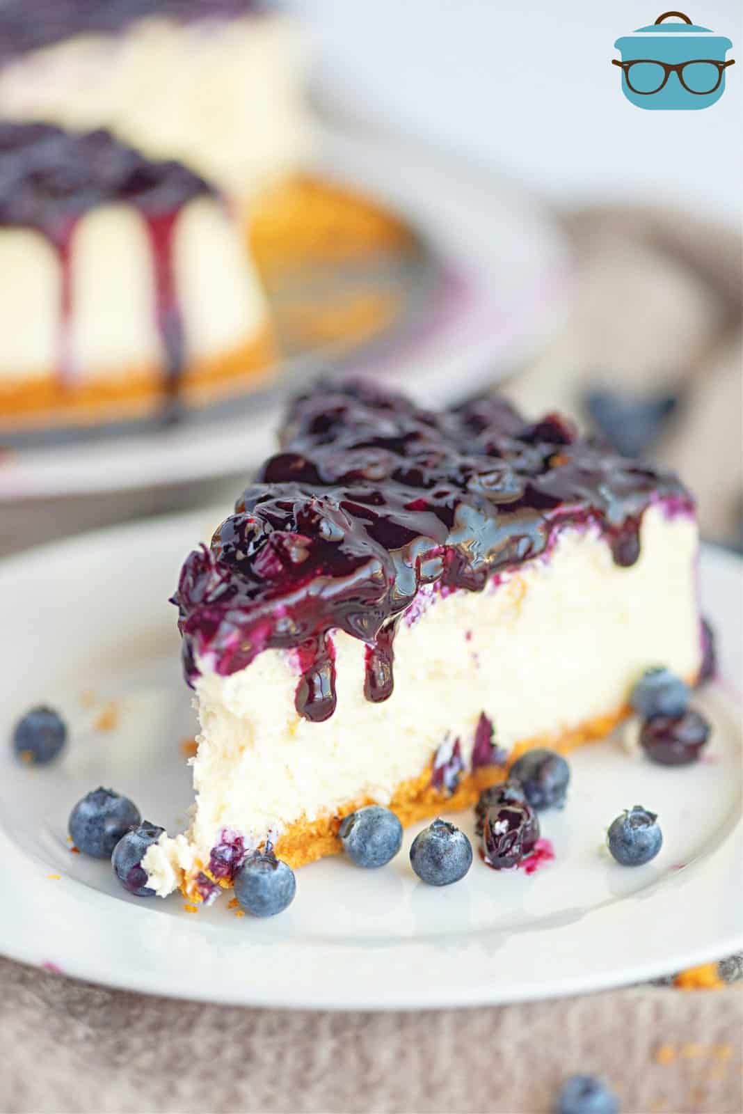 Slice of Blueberry Cheesecake on white plate covered with blueberry sauce.