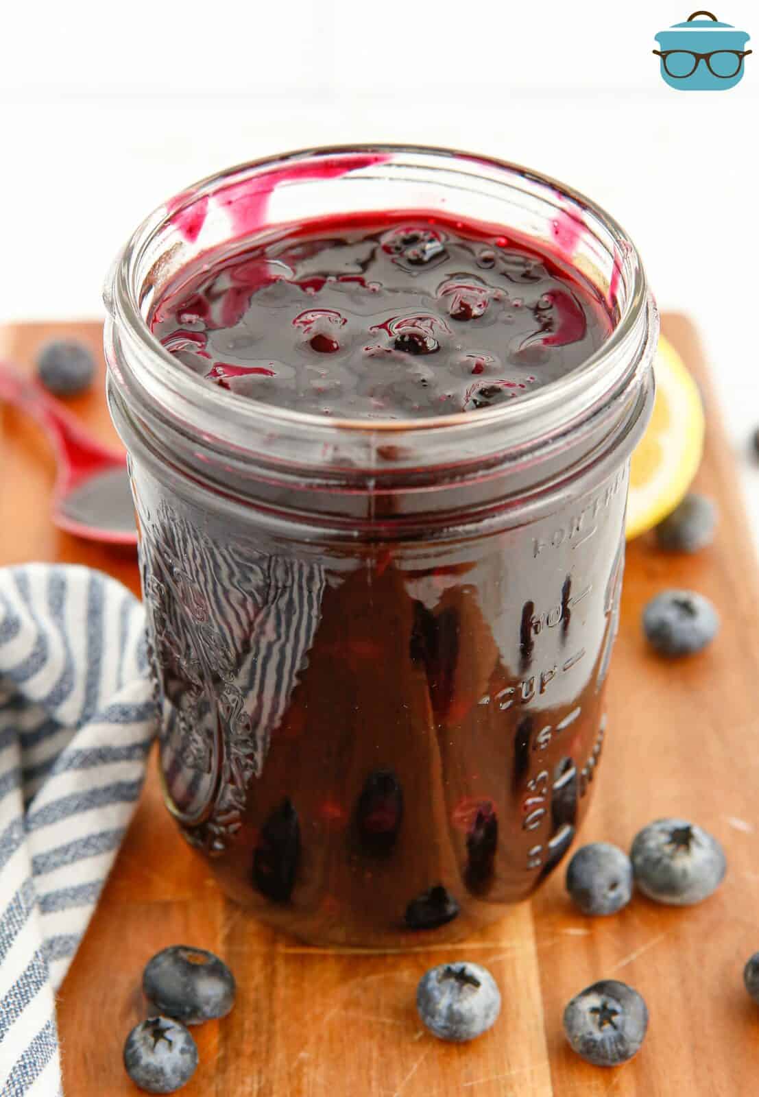 Blueberry Pie Filling in mason jar with blueberries surrounding it.