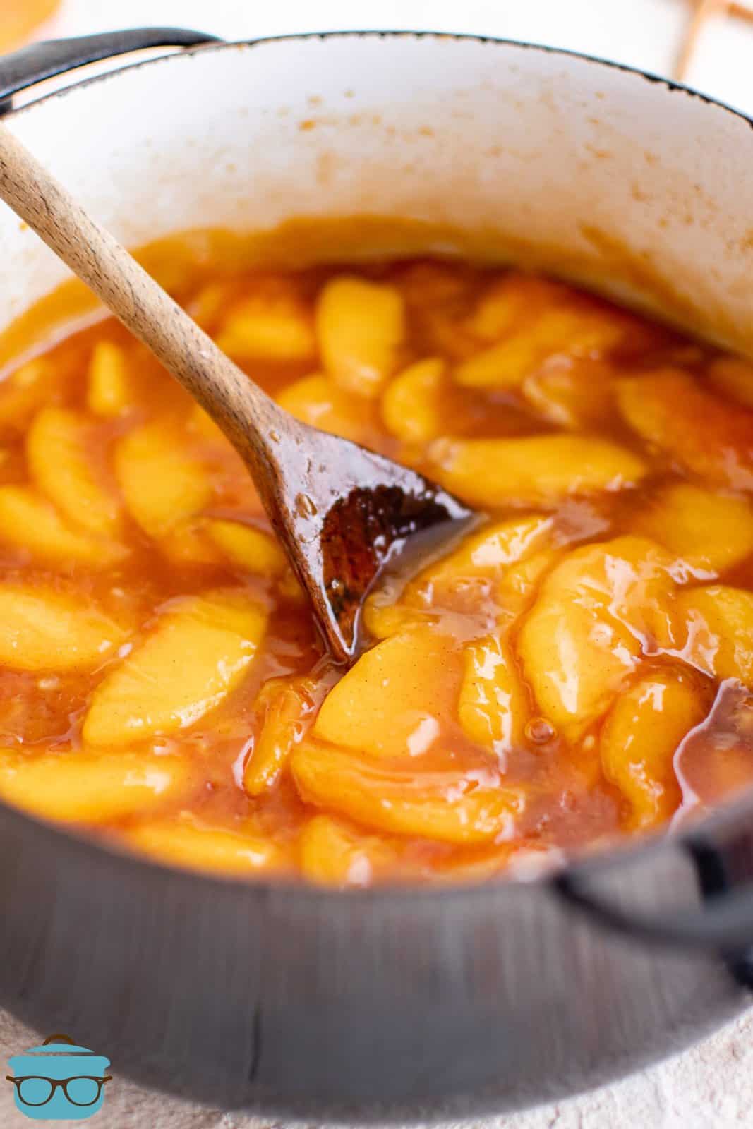 Homemade Peach Pie Filling in large pot with spoon stirring it.