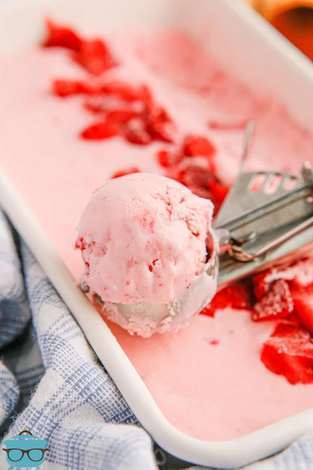 Ice cream scoop with a scoop of No-Churn Strawberry Ice Cream in pan with the rest of ice cream.