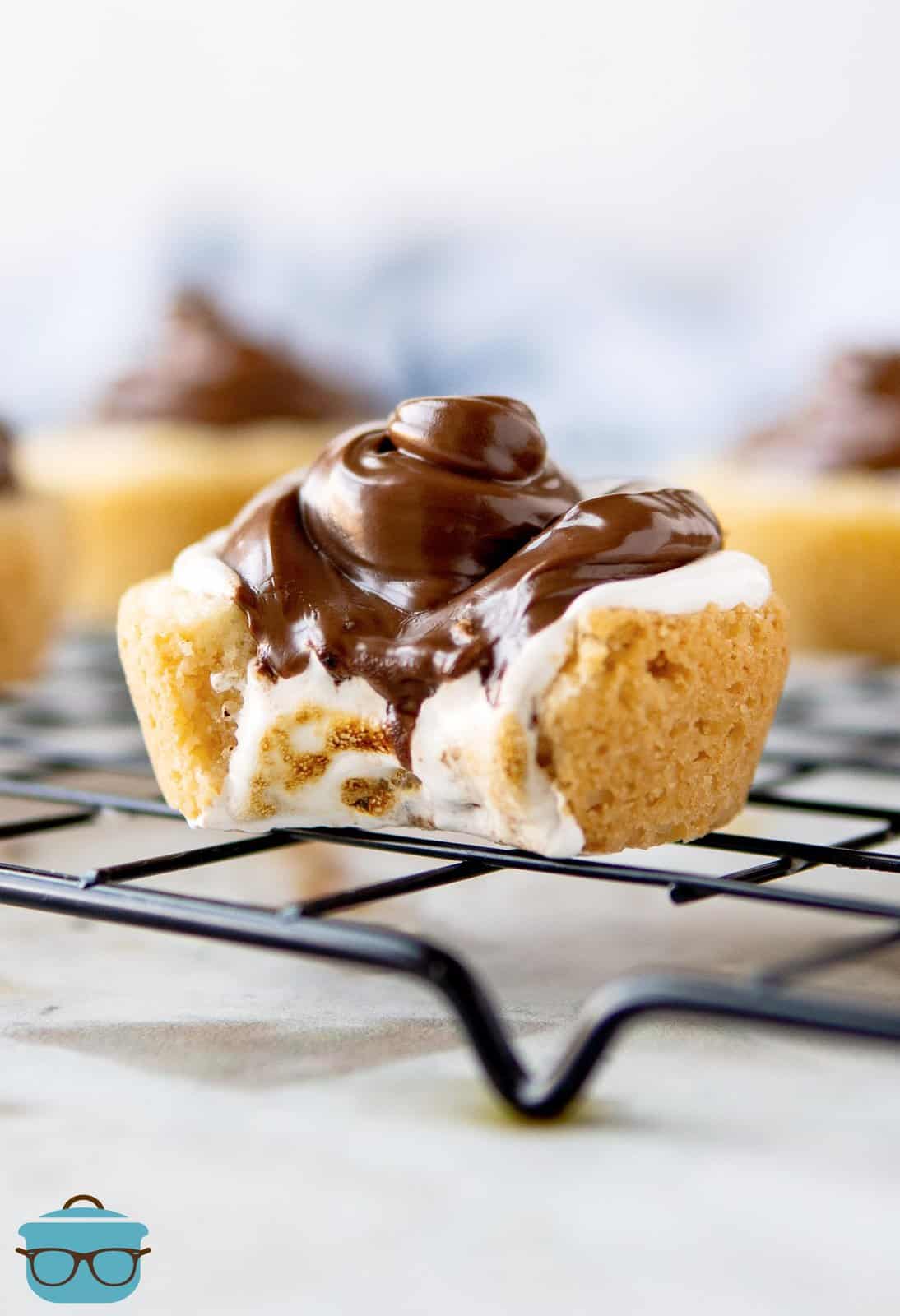 S'mores Cookie Cups on cooling rack with bite taken out showing layers.