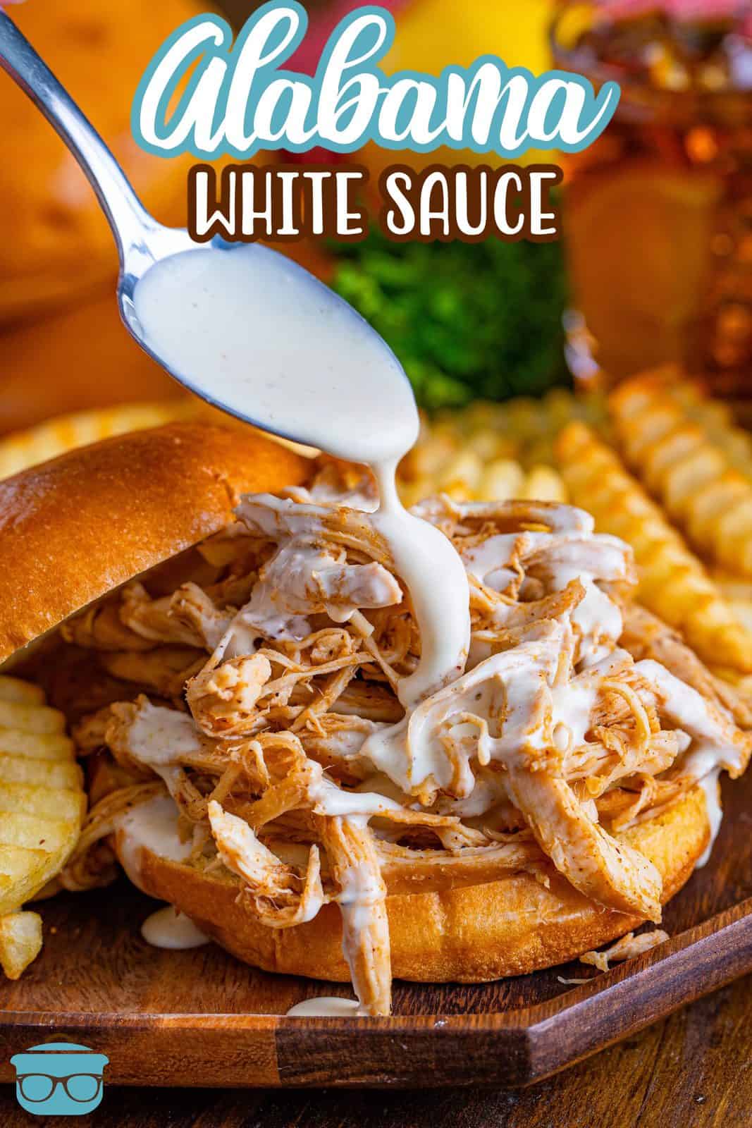 Pinterest image of spoon drizzling Alabama White Sauce over bbq chicken sandwich.