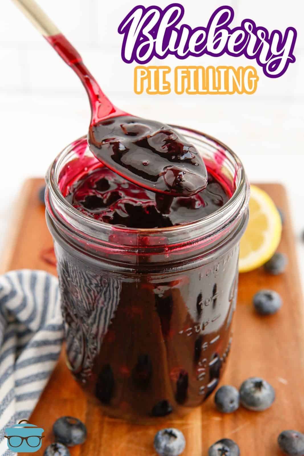 Pinterest image of Blueberry Pie Filling in mason jar with spoon holding some up with blueberries and lemon in background.