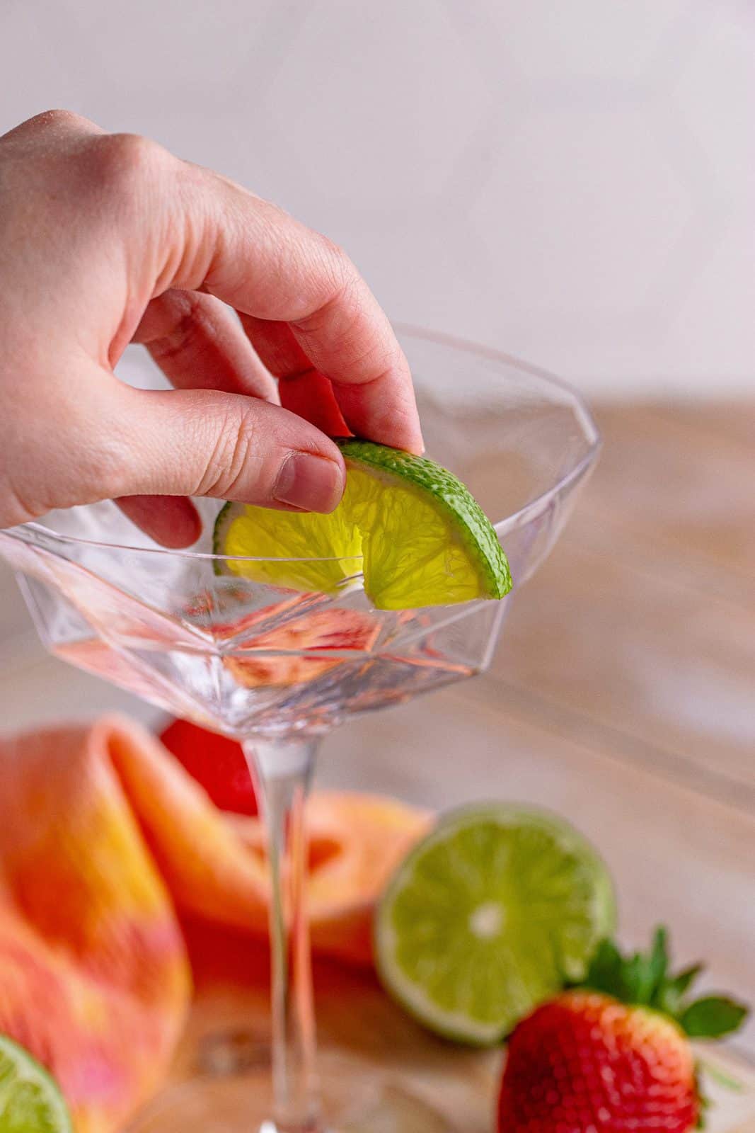 Hand wetting the edges of a glass with a lime wedge.