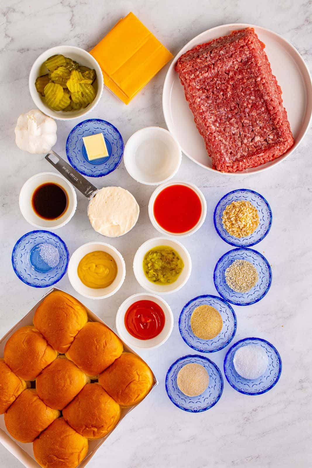 Ingredients needed: mayonnaise, French dressing, dill pickle relish, dried minced onion, granulated sugar, white vinegar, garlic, kosher salt, lean ground beef, Worcestershire sauce, garlic powder, onion powder, Hawaiian slider rolls, American cheese, pickle chips, ketchup, mustard, unsalted butter and sesame seeds.