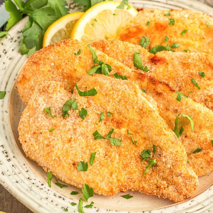 Square image close up of layered Air Fryer Chicken Cutlets on plate with parsley and lemon.