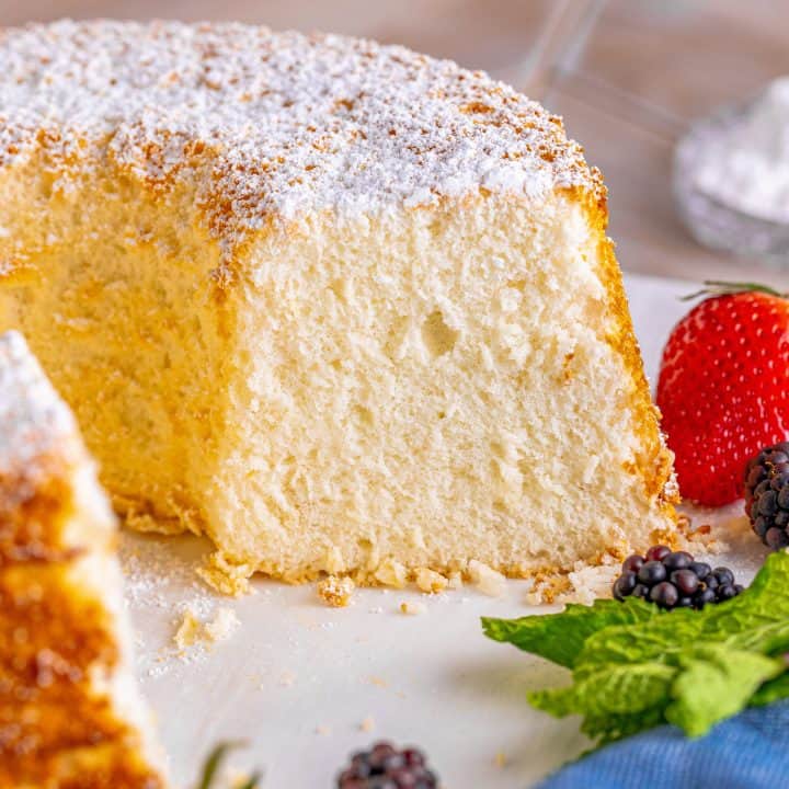 A homemade angel food cake on a white platter with a slice removed.