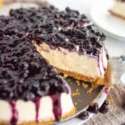 Square image of Blueberry Cheesecake on pan bottom with slices removed.