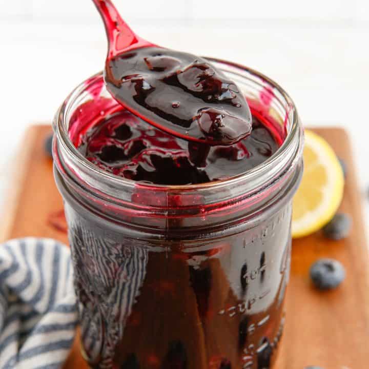 Square image of Blueberry Pie Filling in mason jar with spoon holding some of the filling up.