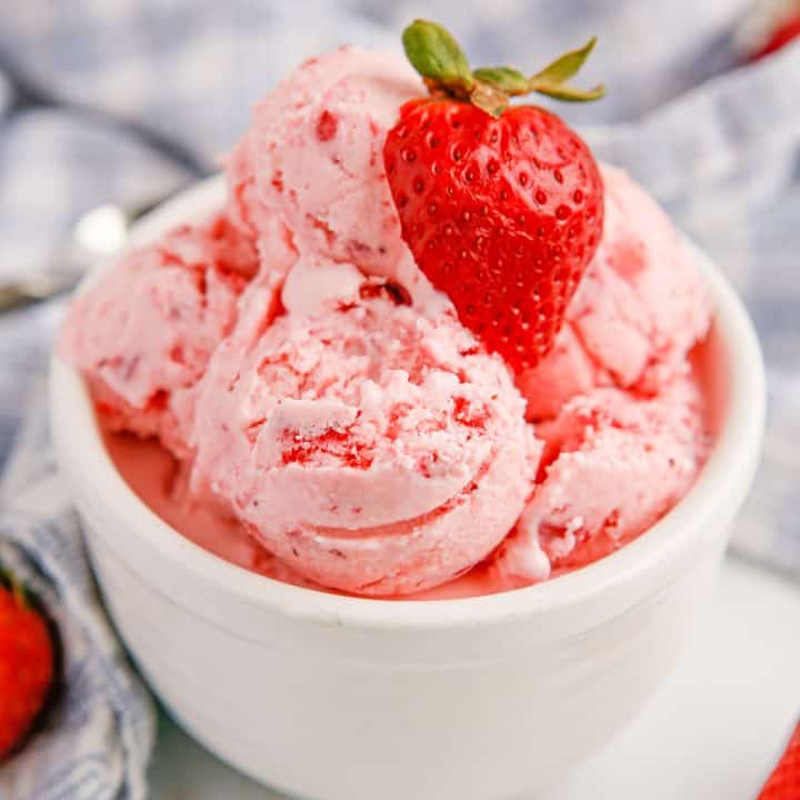 Square image of scoops of No-Churn Strawberry Ice Cream in white bowl garnished with a sliced strawberry.