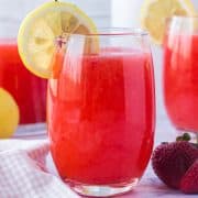 Square close up image of Strawberry Lemonade in glass with garnishes.