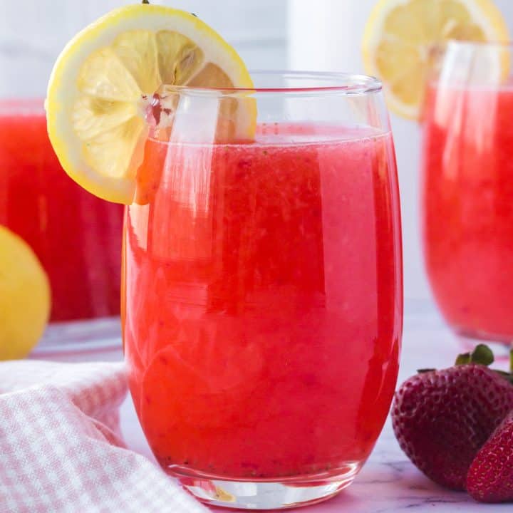 Square close up image of Strawberry Lemonade in glass with garnishes.