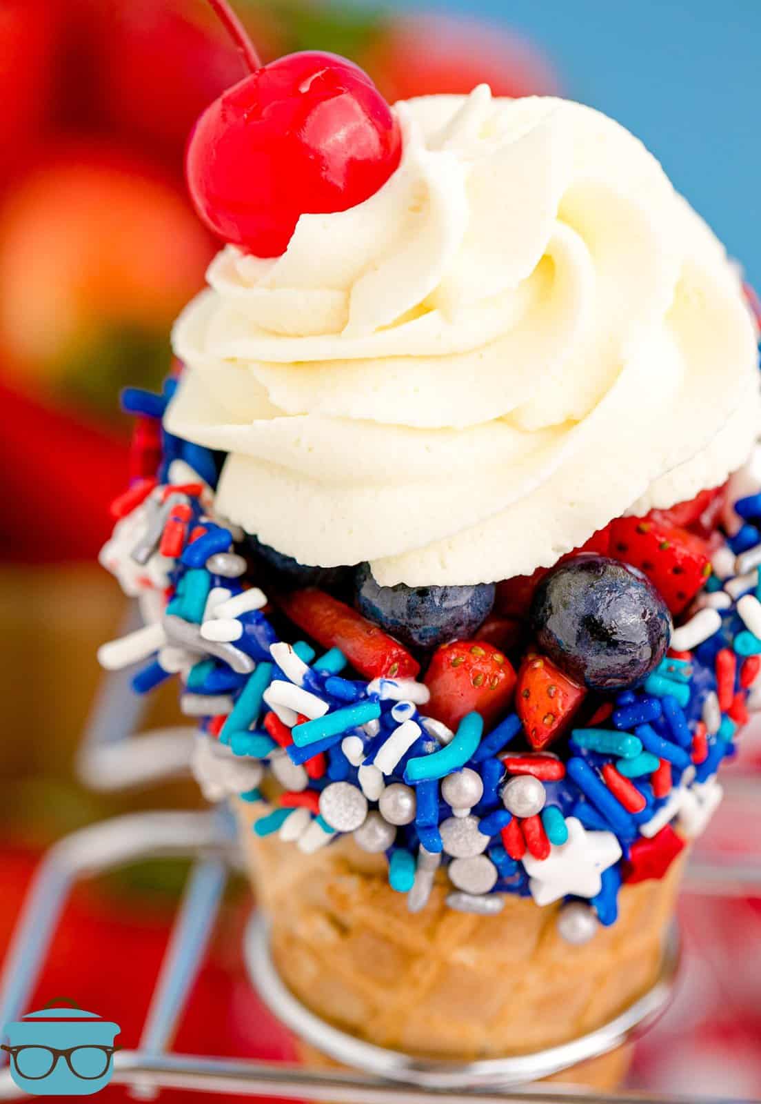 Close up of 4th of July Waffle Cones in cone holder with whipped topping and cherry.