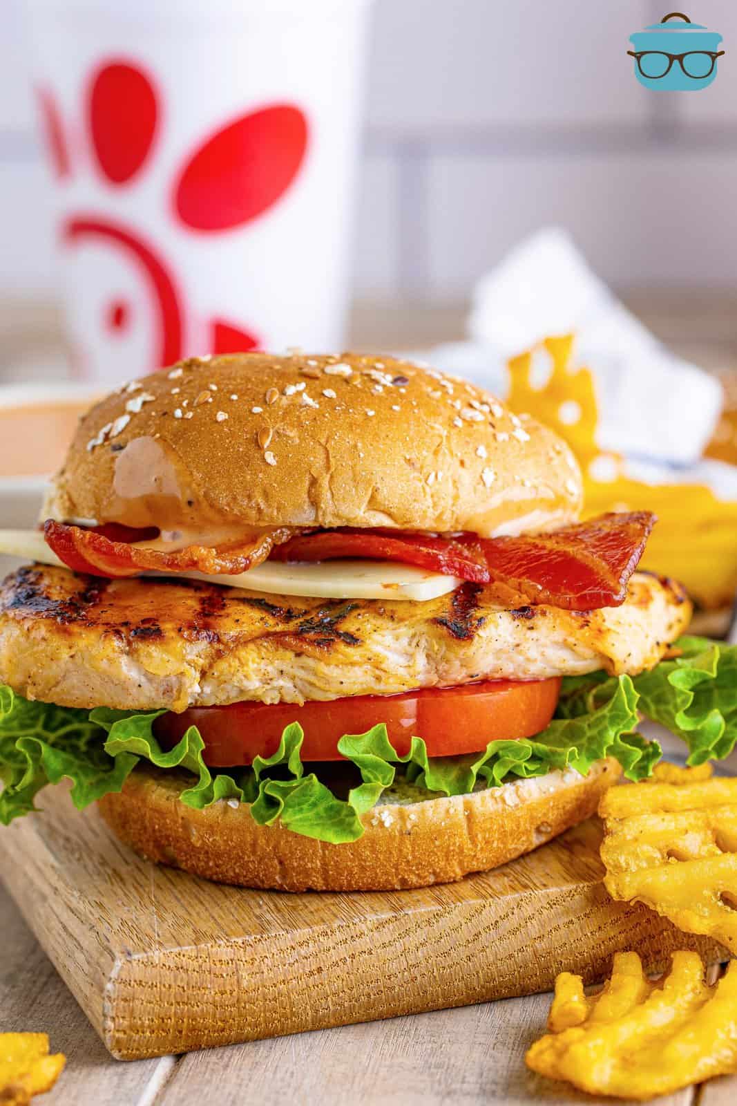 Chick-fil-A Grilled Chicken Club Sandwich on wooden board with waffle fries next to it.